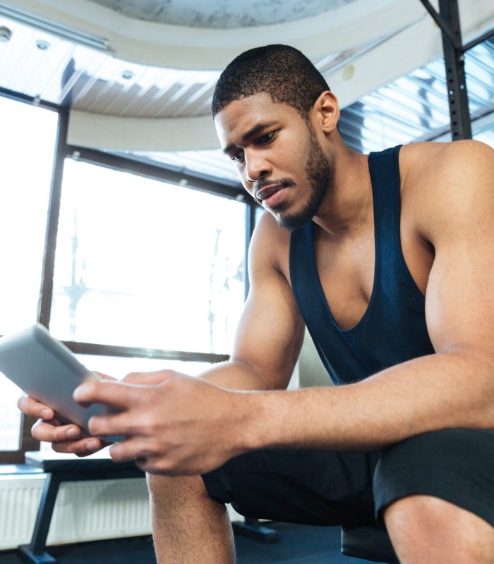 Afro american fitness man using tablet computer in the gym