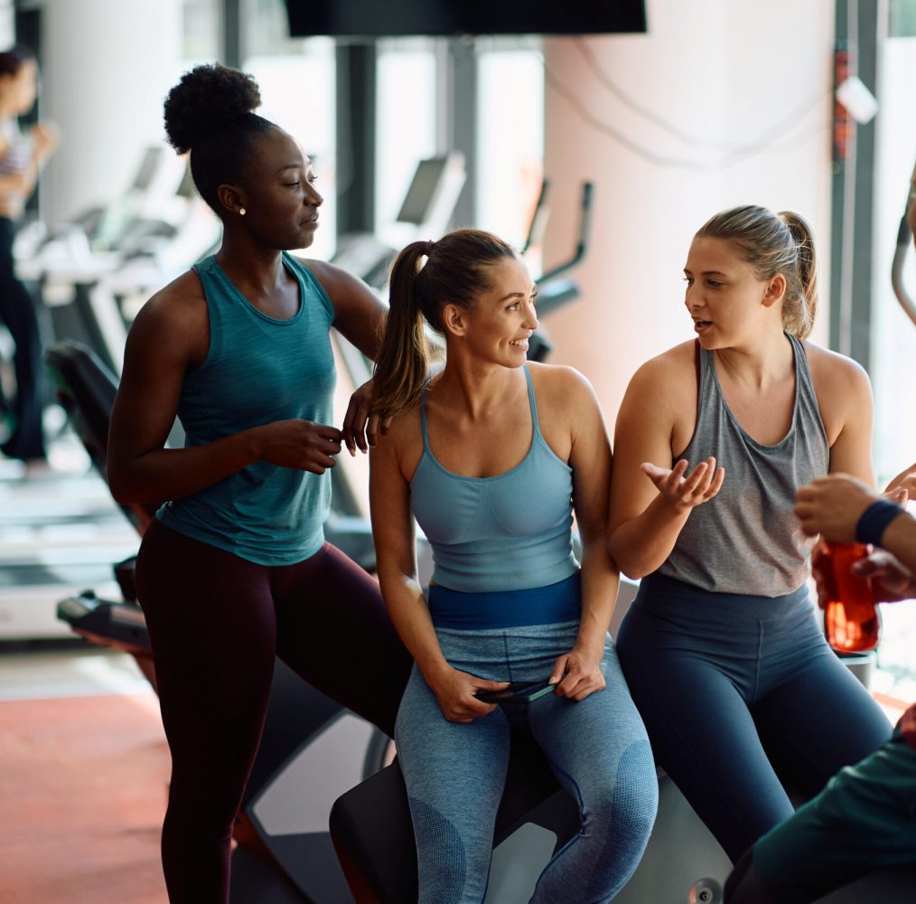 Multiracial group of athletic people communicating while relaxing after sports training in a gym.