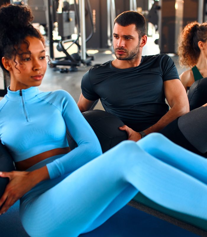 Slim women african american and caucasian ethnicity and muscular man in sportswear doing exercises with a heavy medicine ball on a rubber mat in a gym club. The concept of sports and recreation.